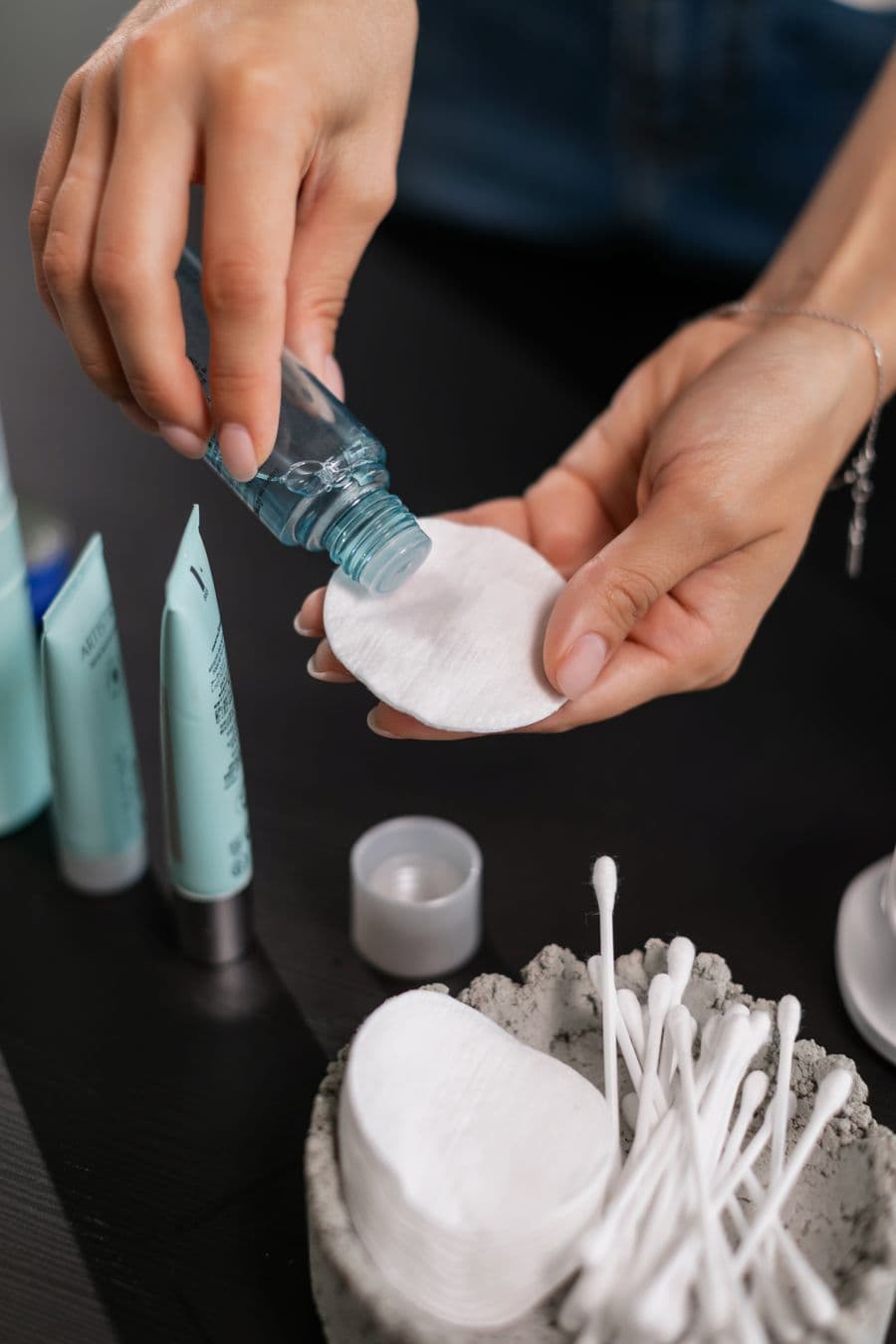 Đôi tay rót toner lên bông trong một bước chăm sóc da hằng ngày